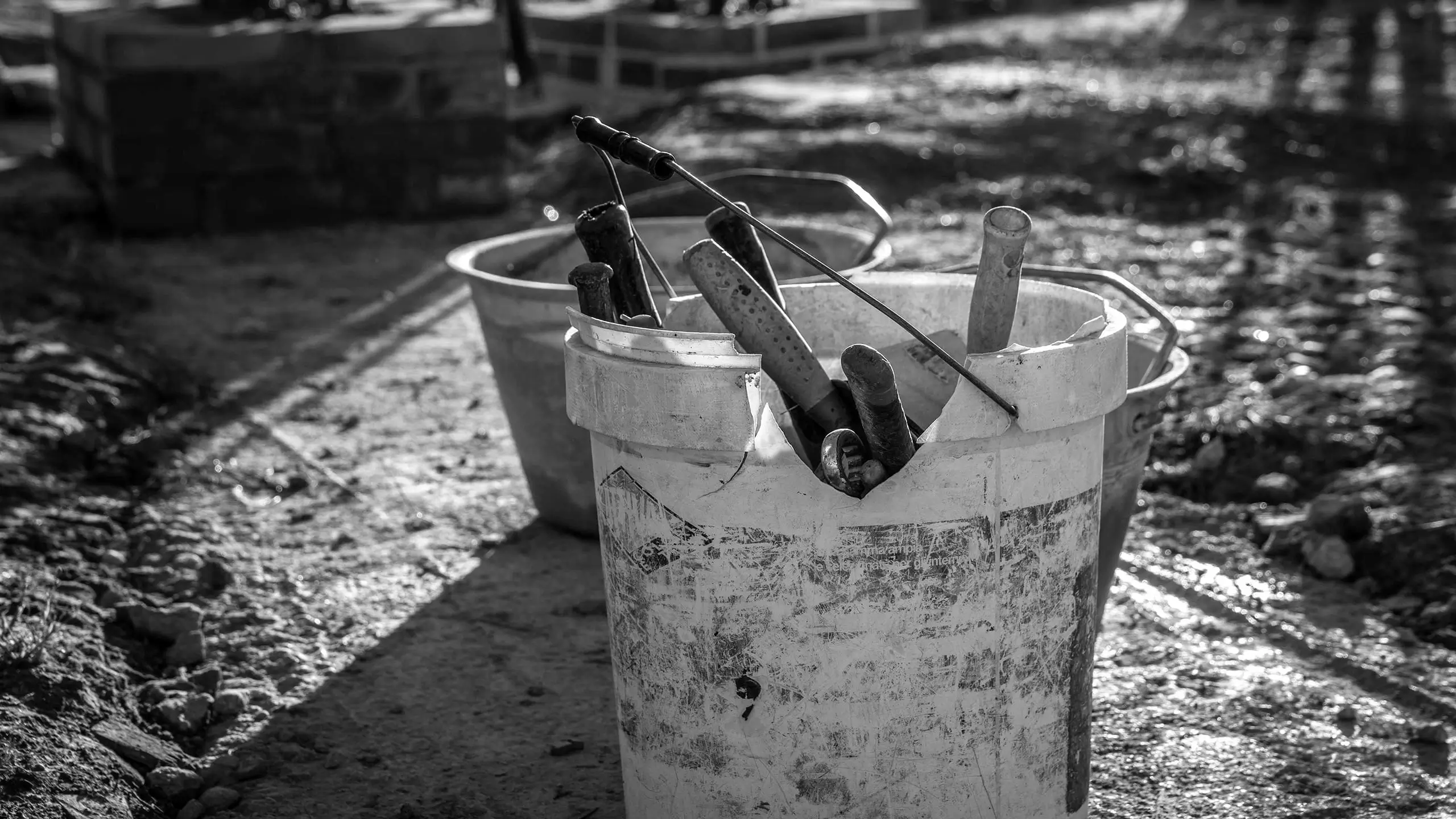 Secchi da cantiere consumati con attrezzi da muratore all’interno, in primo piano su un fondo di terra, simbolo del lavoro quotidiano dell’impresa edile.