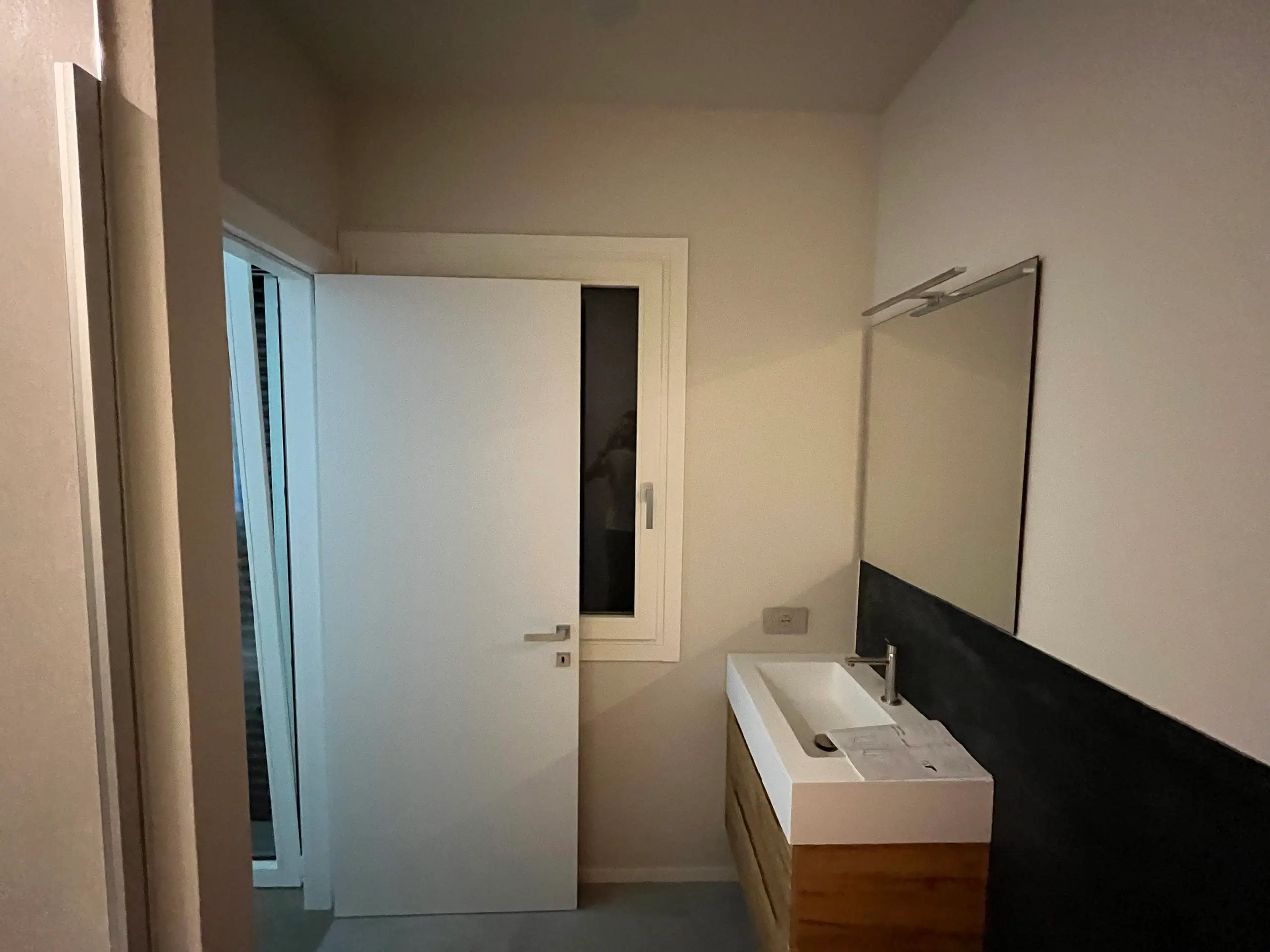 Bagno moderno dopo ristrutturazione Casa C.S.: lavabo sospeso in legno, parete nera, specchio ampio e porta scorrevole in ambiente luminoso minimal.