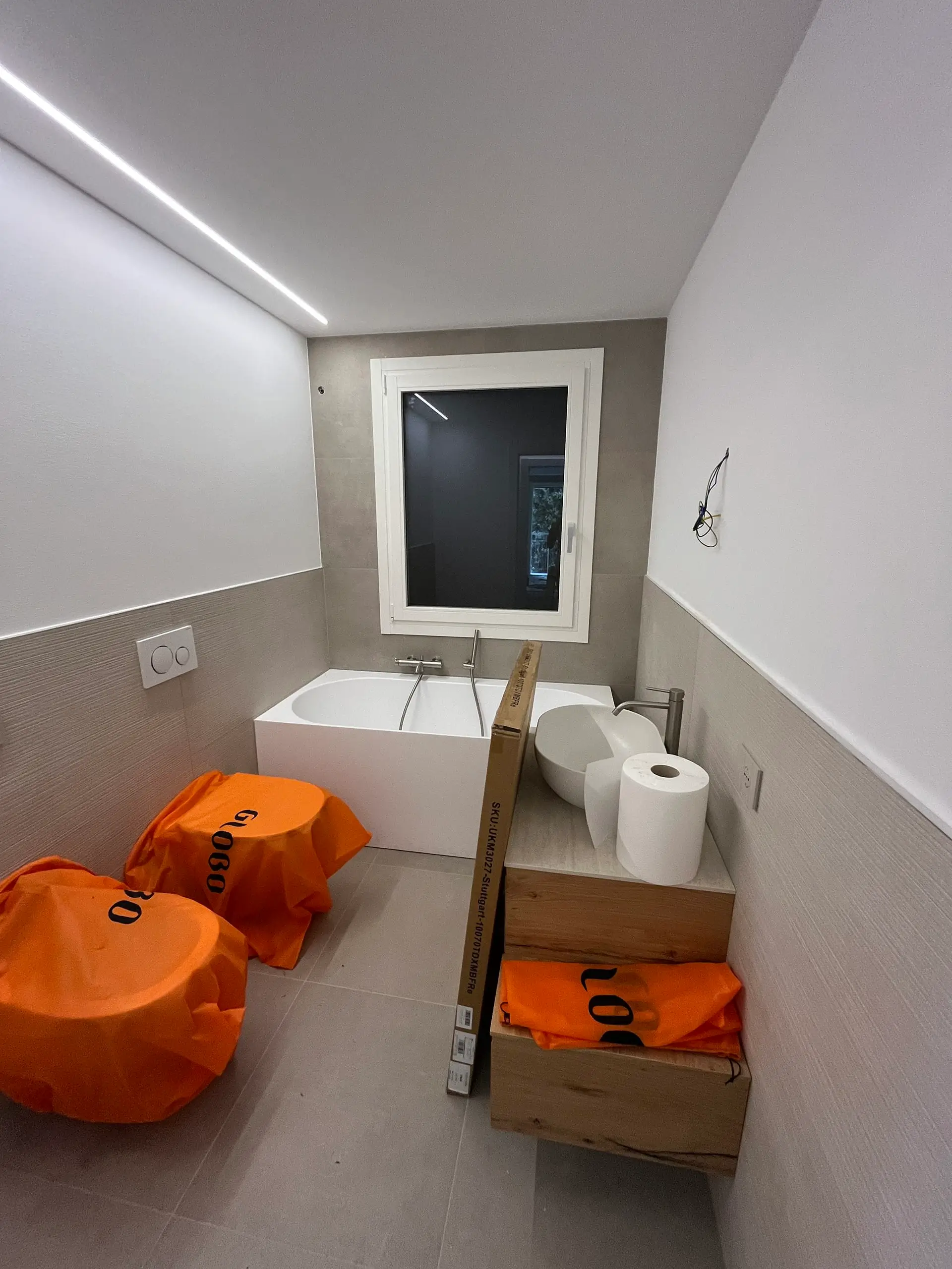 Vasca da bagno installata dopo ristrutturazione Casa C.S.: piatto doccia vasca con rubinetteria, illuminazione led soffitto, piastrelle grigie e packaging protettivo.