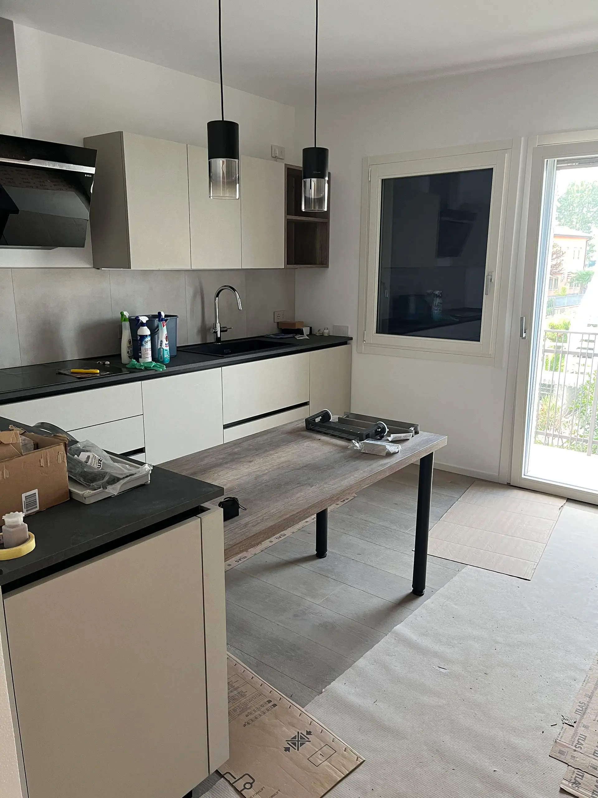 Cucina completata dopo ristrutturazione Casa C.S.: pensili beige con cappa nera, piano in legno grezzo, lavello e finestra panoramica su balcone.