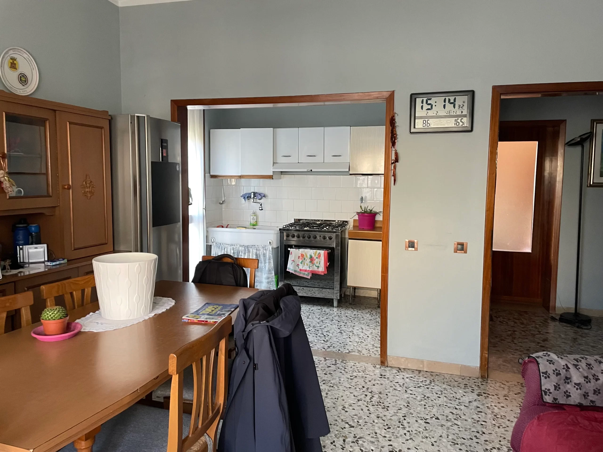 Cucina abitabile pre ristrutturazione di Casa C.S. con tavolo in legno, pensili bianchi bianchi, frigo, fornelli e pavimento in ceramica in ambiente rustico.