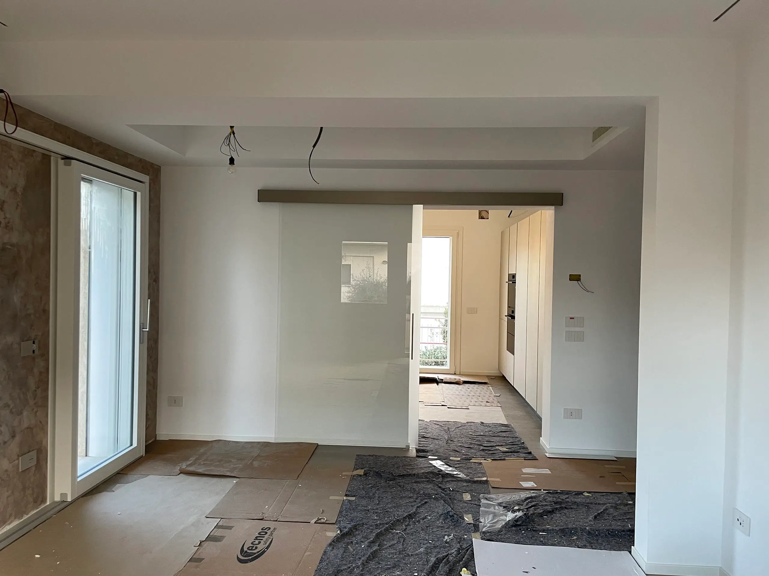 Zona giorno dopo ristrutturazione Casa C.S.: living open space con porte scorrevoli in vetro, cucina moderna e pavimento protetto in fase finale lavori.