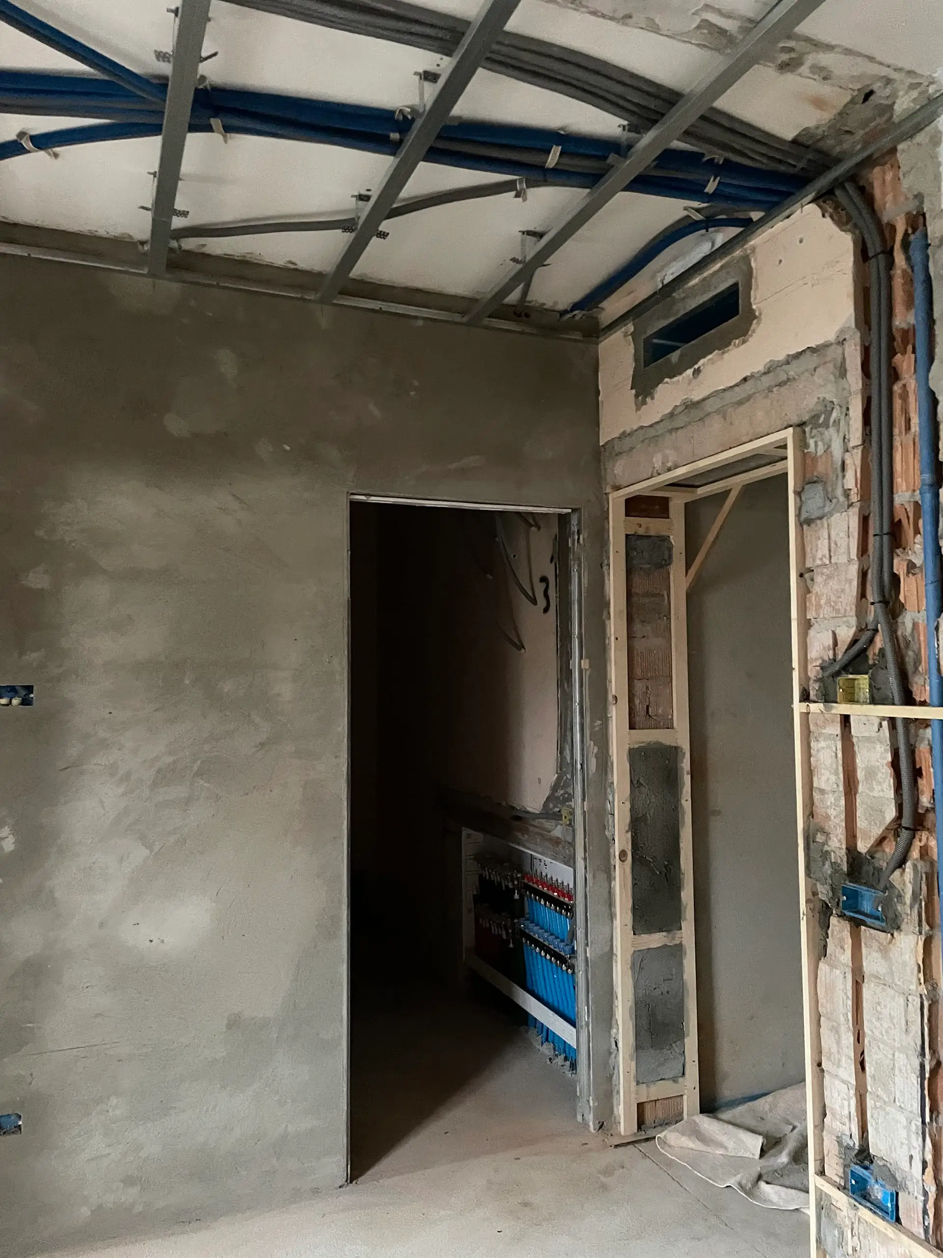 Rifacimento impianti elettrici e idraulici WIP Casa C.S.: tubi blu a vista, griglie metalliche soffitto, quadri elettrici e porte incomplete in cantiere.